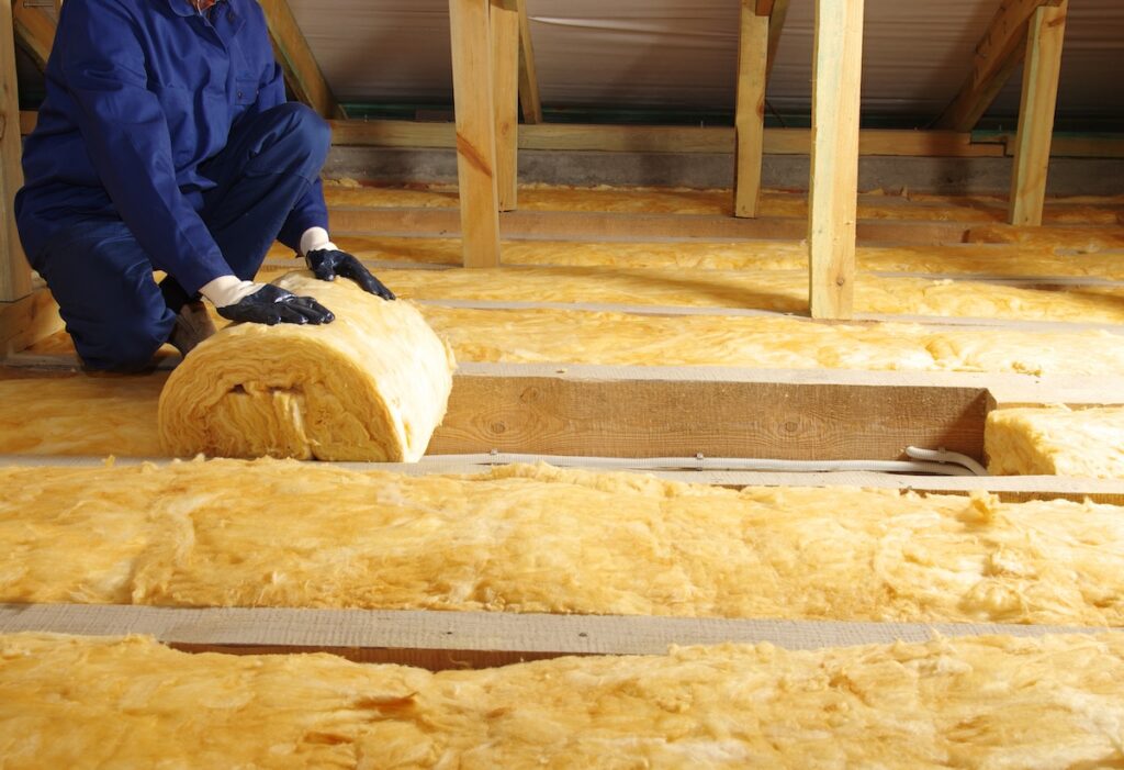 Construction worker thermally insulating house attic with fiberglass