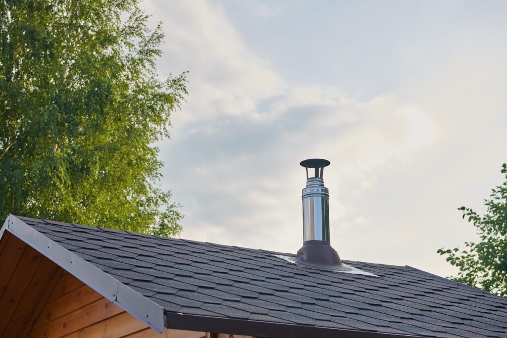 Stainless steel metal chimney pipe on the roof of the house against the sky.