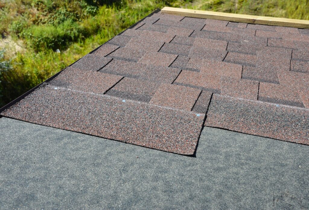 Installing brown dimensional asphalt roof shingles on the underlayment, water-resistant, waterproof protection barrier material on the rooftop of the house