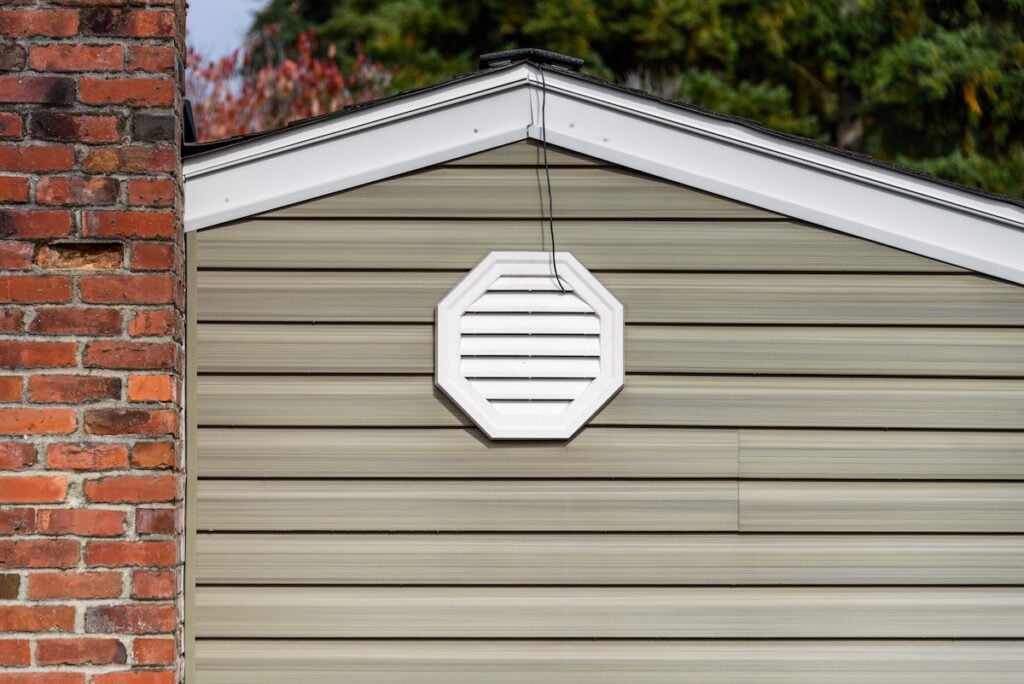 Exterior wall of suburban house, old brick chimney, attic fan exhaust vent on wall