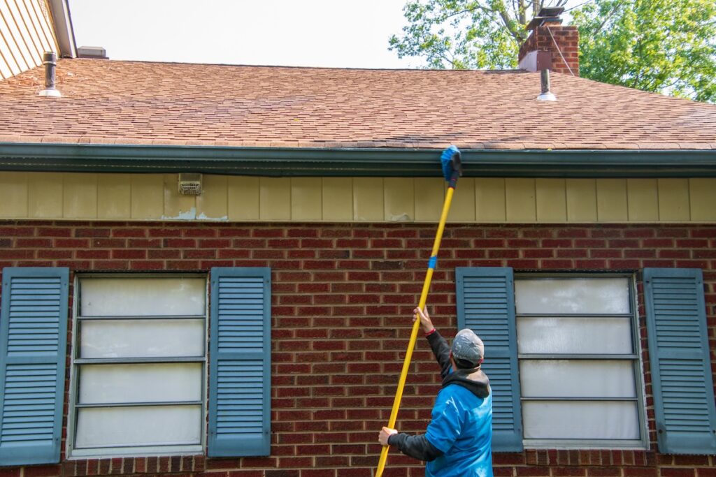 cleaning the soffit of a house with a brush on a long pole