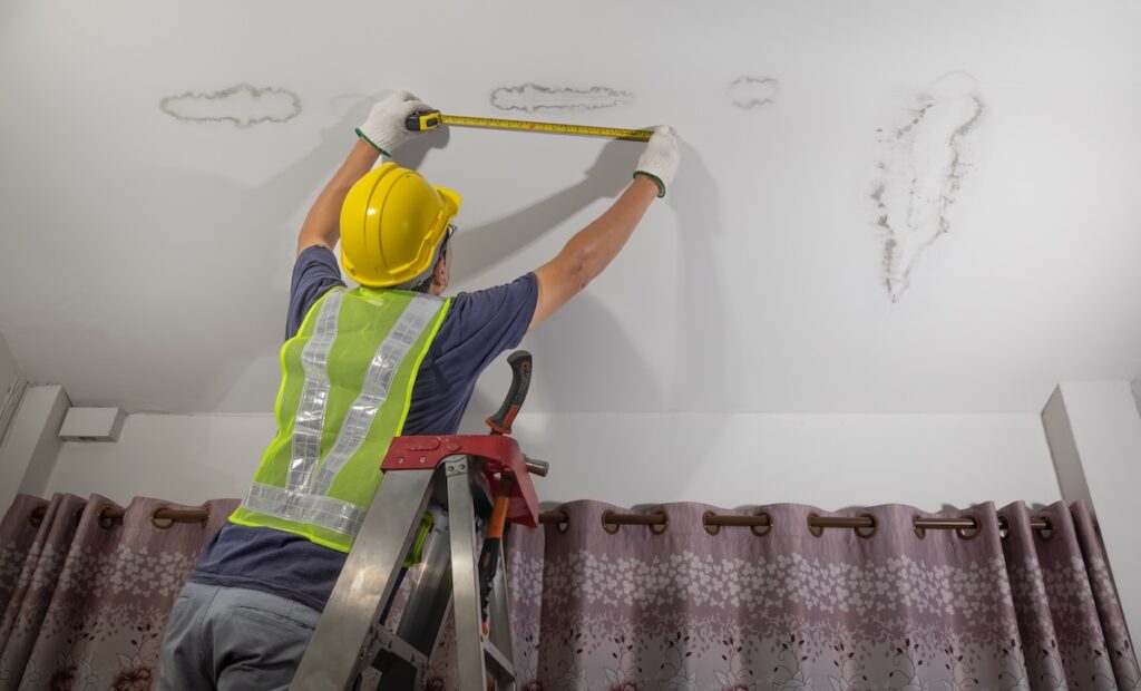 Worker measuring water stain on ceiling