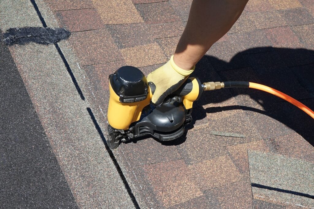 A new roof cover protection being applied. A roofer nailing shingles with air gun.