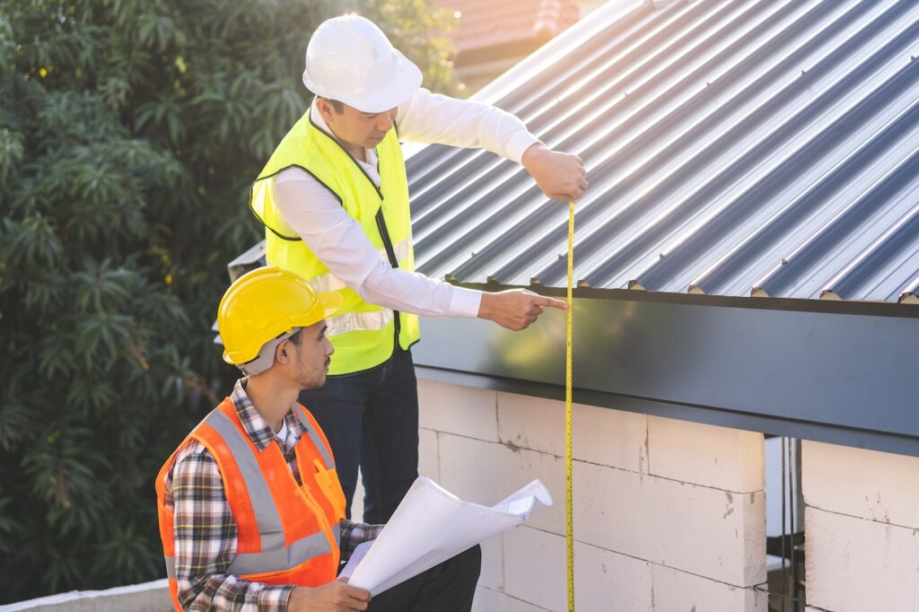 Builder team, foreman house asian young engineer, architect, contractor discussing metal sheet rooftop on blueprint follow project to build industrial plan at outdoor site. Engineering worker people.