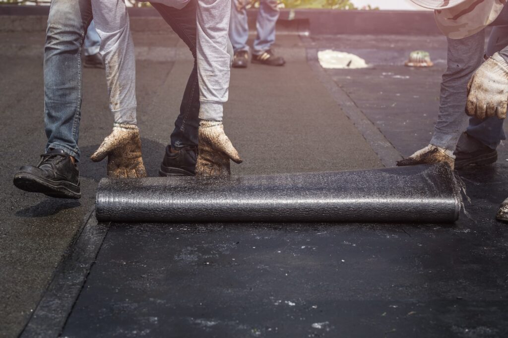 Group of worker installing tar foil on the rooftop of building. Waterproof system by gas and fire torching