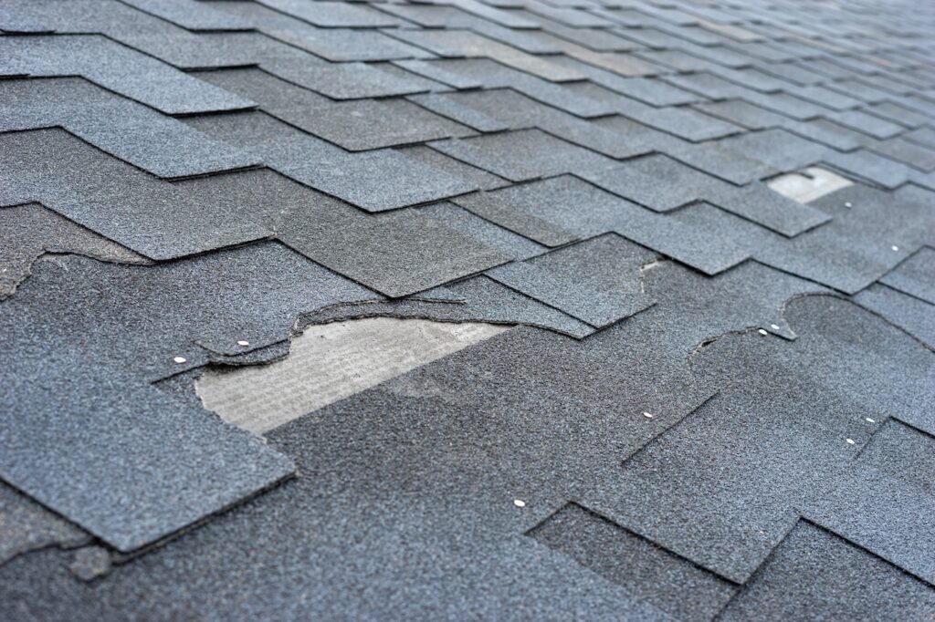 Сlose up view of asphalt shingles roof damage that needs repair.